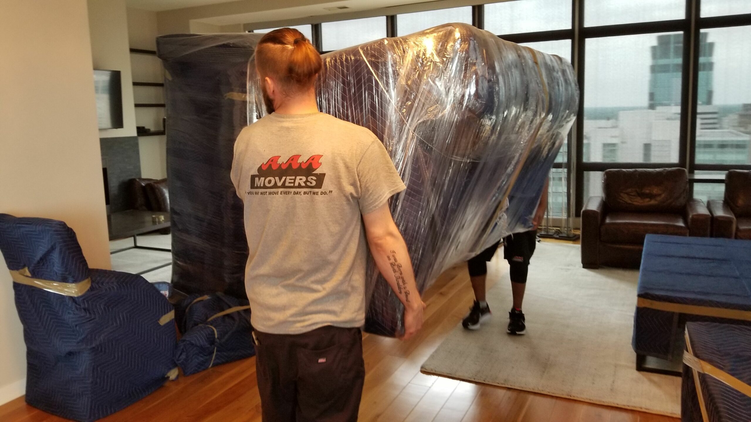 Movers carrying a couch that has been wrapped with a blanket and plastic wrap