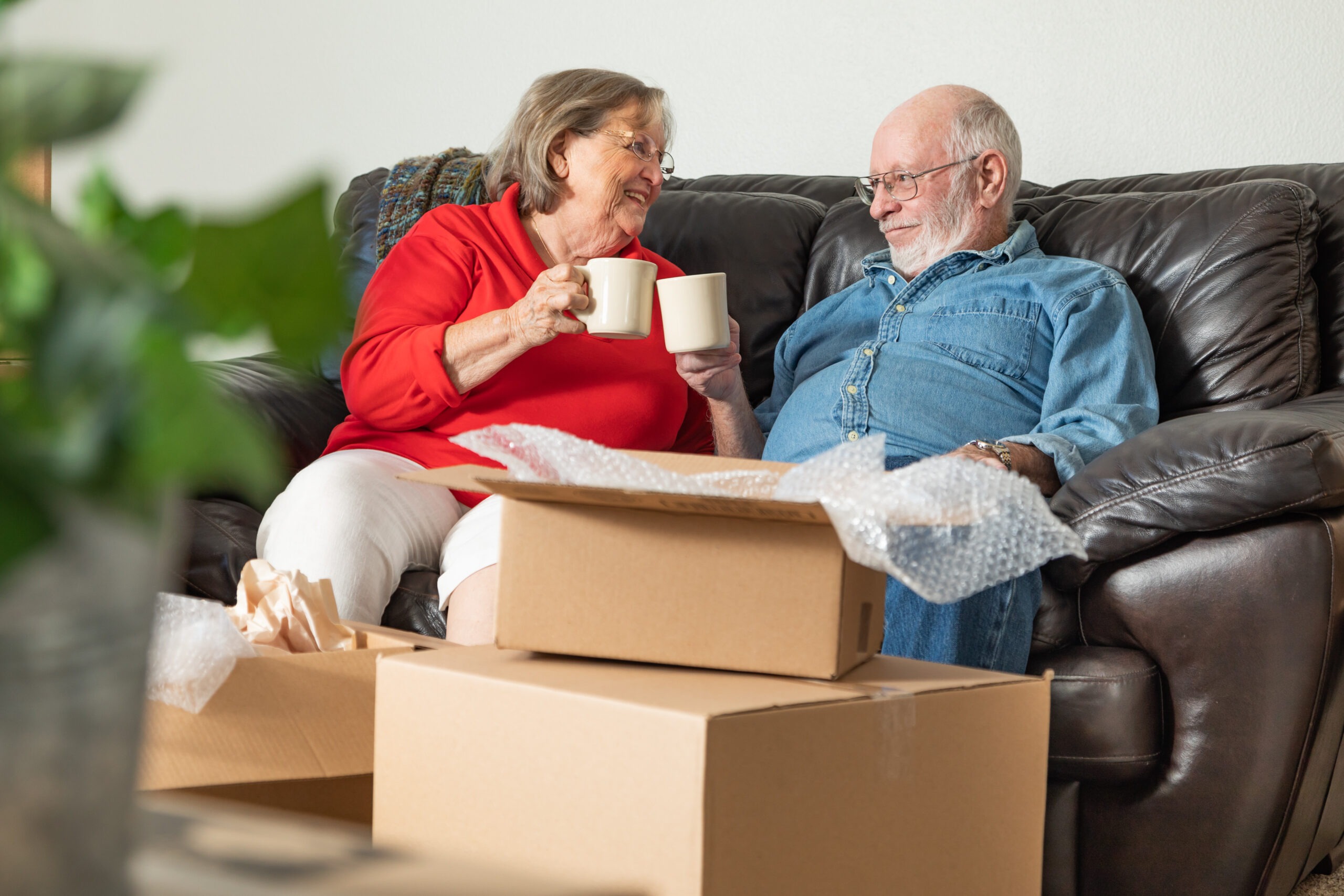 Senior Adult Couple Resting on Couch with Cups of Coffee Surrounded with Free Moving Boxes.