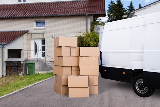 A stack of moving boxes on a driveway next to a moving van