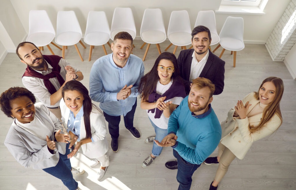 Diverse team of happy business people in St. Paul, Minnesota standing together and applauding. Group portrait of young male and female colleagues looking up at camera, smiling and clapping hands. High angle, shot from above